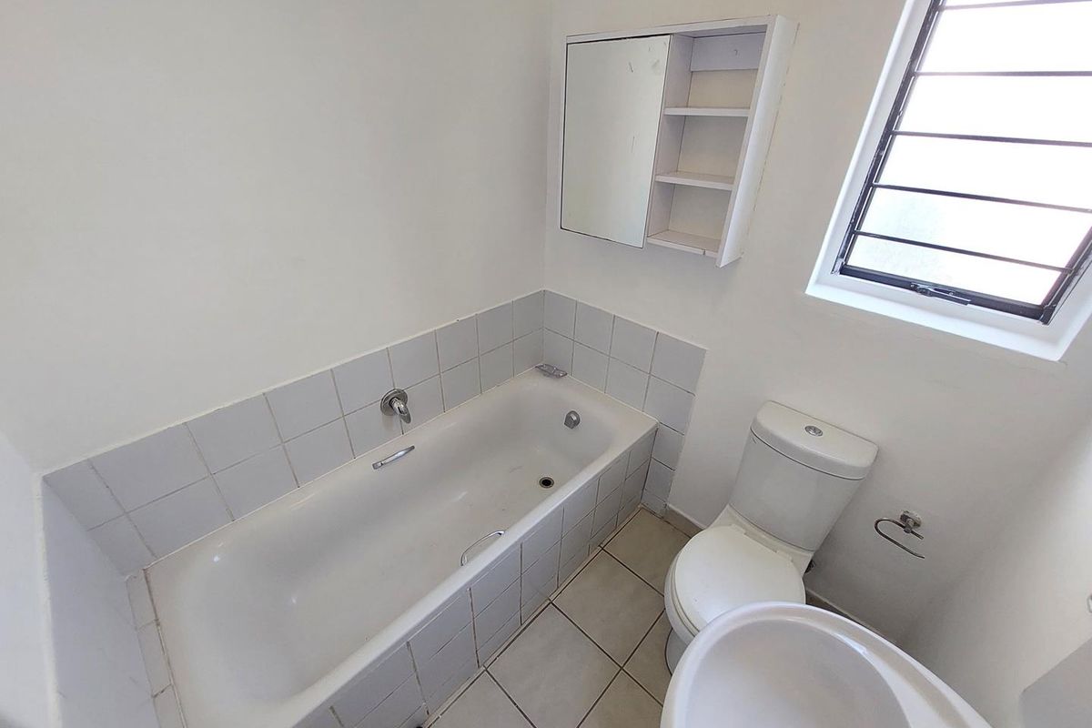 A functional bathroom featuring a built-in bathtub with tiled surround, a standard toilet, a pedestal basin, and a wall-mounted medicine cabinet.