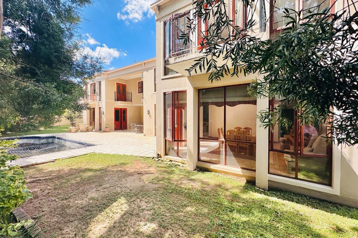 Rear view of a two-story house featuring a paved patio, swimming pool, and large glass windows overlooking the garden area.