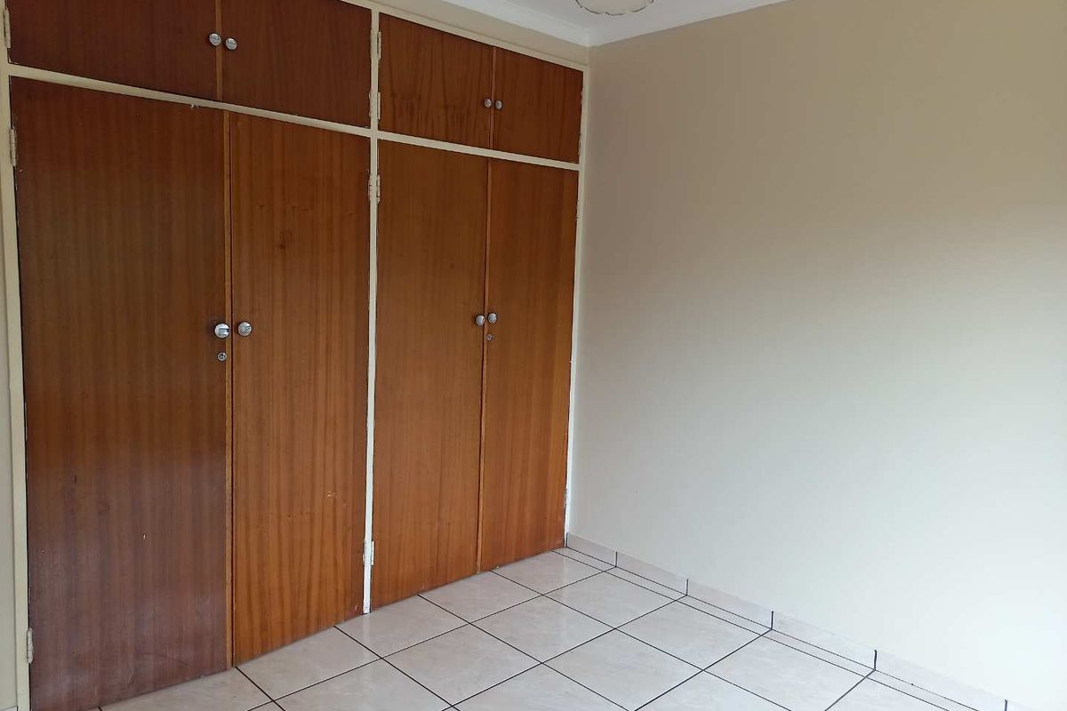 A bedroom featuring built-in wooden cupboards and tiled flooring, offering a clean and functional space.