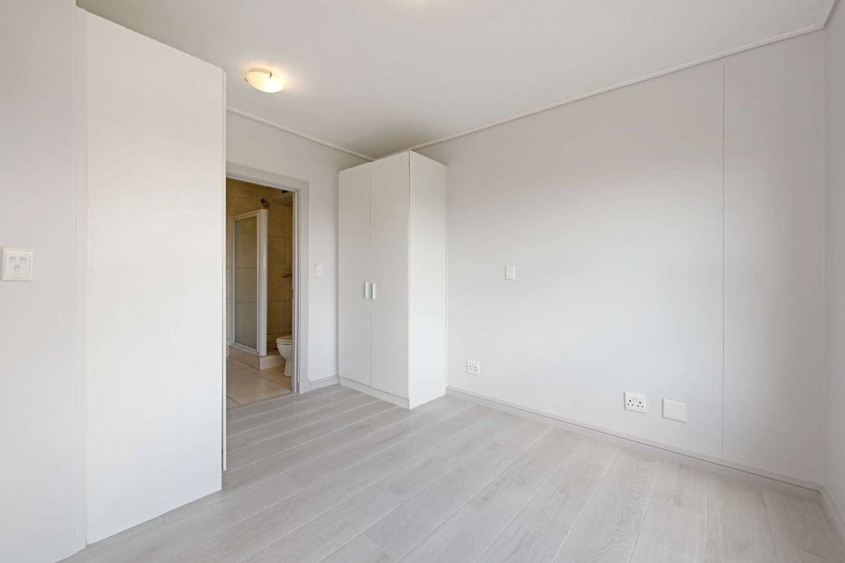 A bright, neutral bedroom featuring light-toned laminate flooring, built-in cabinetry, and direct access to an en-suite bathroom.