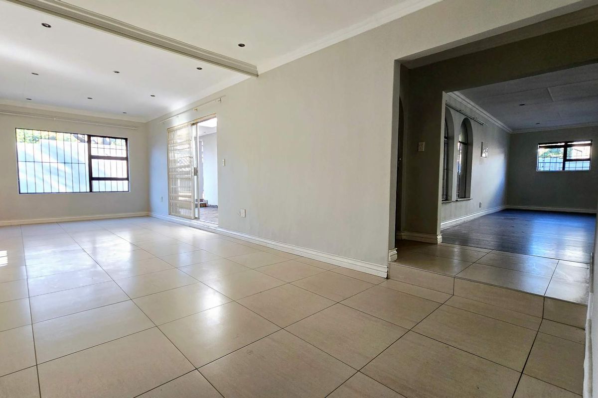 Spacious, open-plan living area featuring neutral tiled flooring, recessed lighting, and large windows with security bars, offering a bright and versatile living space.