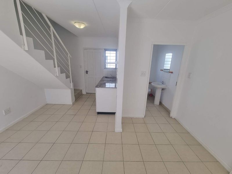 Open plan living area featuring a kitchenette, staircase, and adjacent bathroom with a pedestal sink, finished with neutral floor tiles.