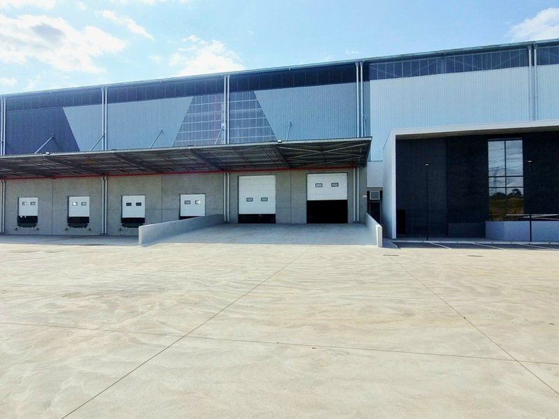 Modern industrial warehouse facility featuring multiple loading docks with roller shutter doors, a large concrete hardstand area, and contemporary metal cladding.