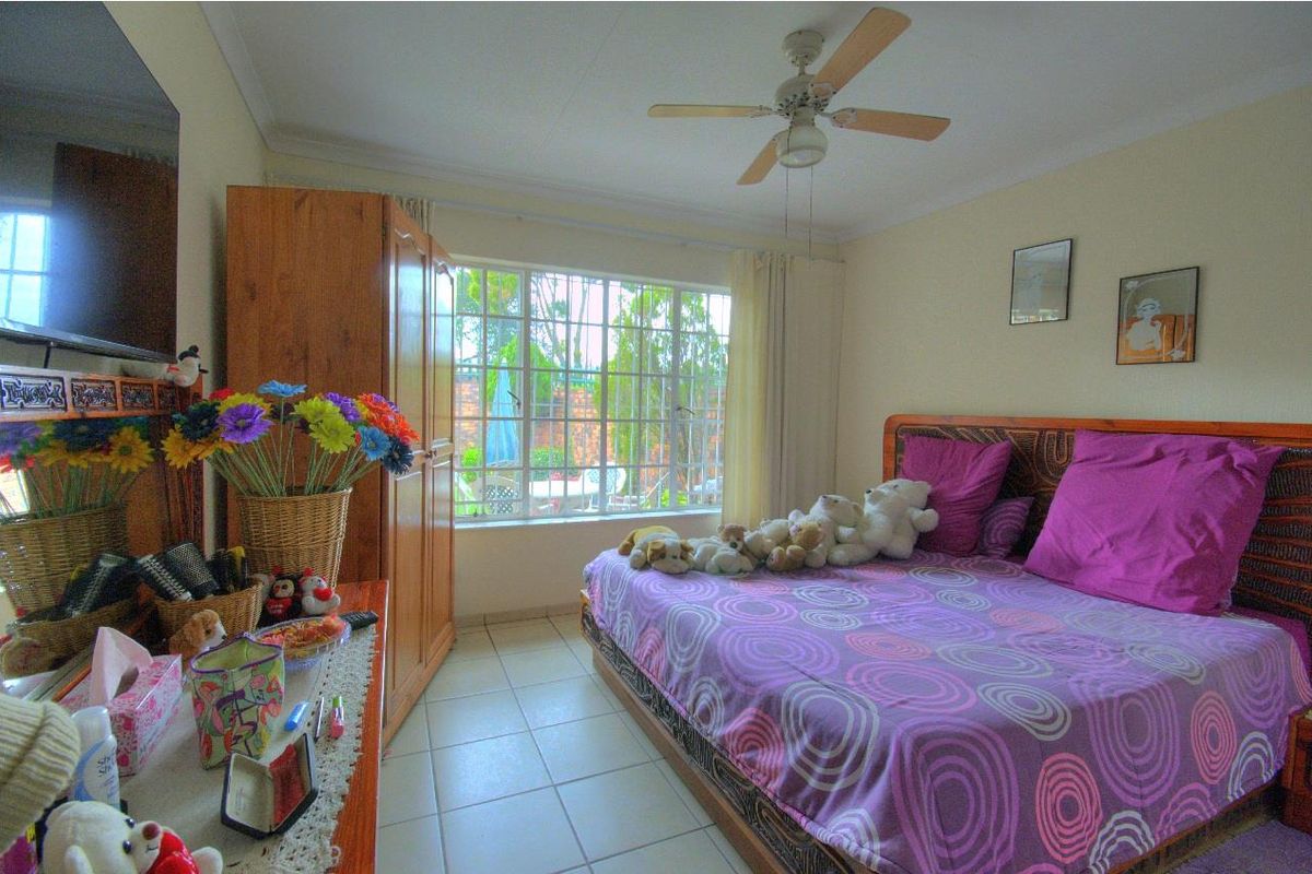 A bedroom featuring tiled flooring, a ceiling fan, and a large window providing natural light and a view of the rear garden area.