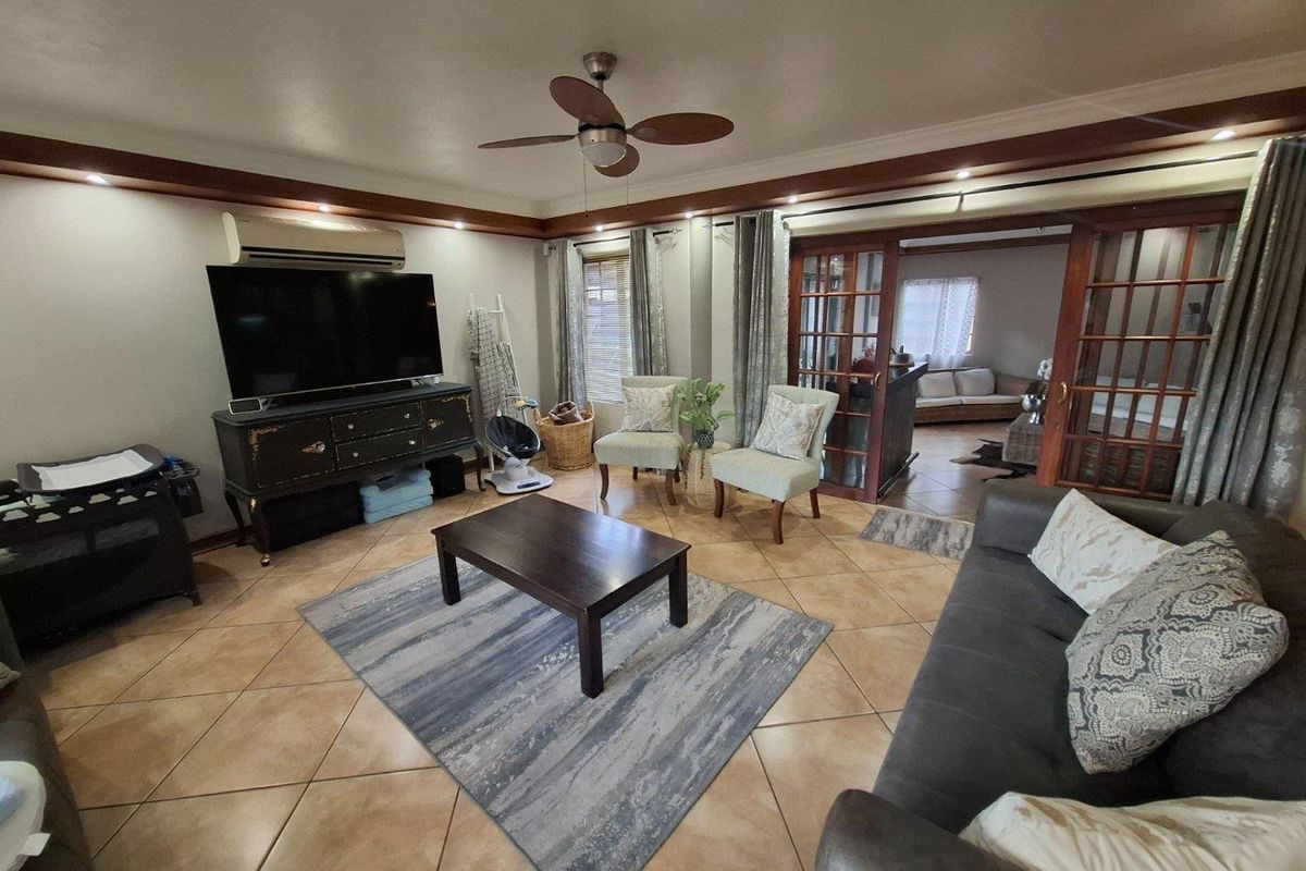 Spacious living room featuring ceramic floor tiles, a ceiling fan, and timber-framed glass doors leading to an adjacent room.