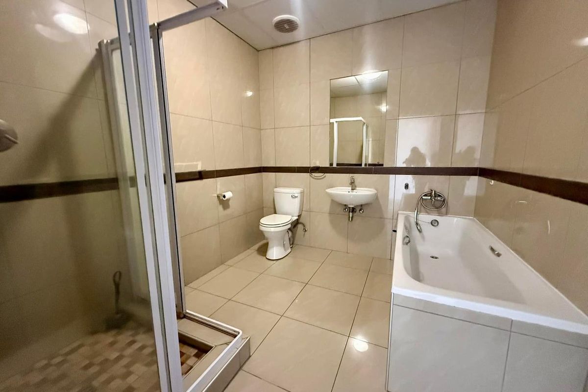 A spacious bathroom featuring a separate shower enclosure, bathtub, wall-mounted basin, and toilet, finished with neutral floor-to-ceiling wall tiles.