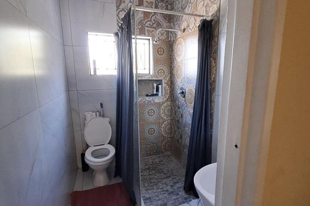 A compact bathroom featuring a walk-in shower with decorative patterned tiling, a standard toilet, and a wall-mounted basin.