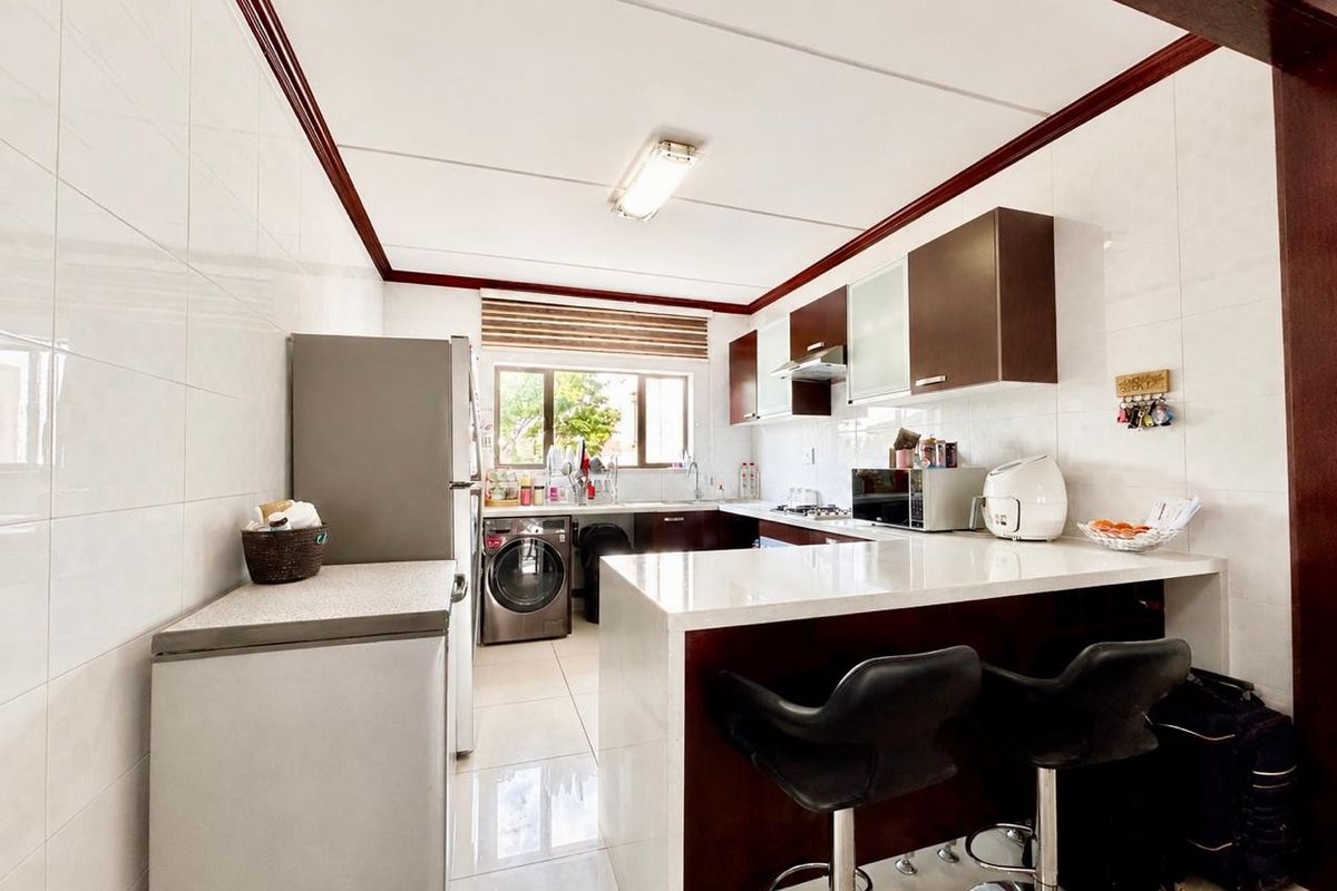 A functional kitchen featuring dark wood cabinetry, stone countertops, a breakfast bar, and integrated appliances with tiled finishes throughout.
