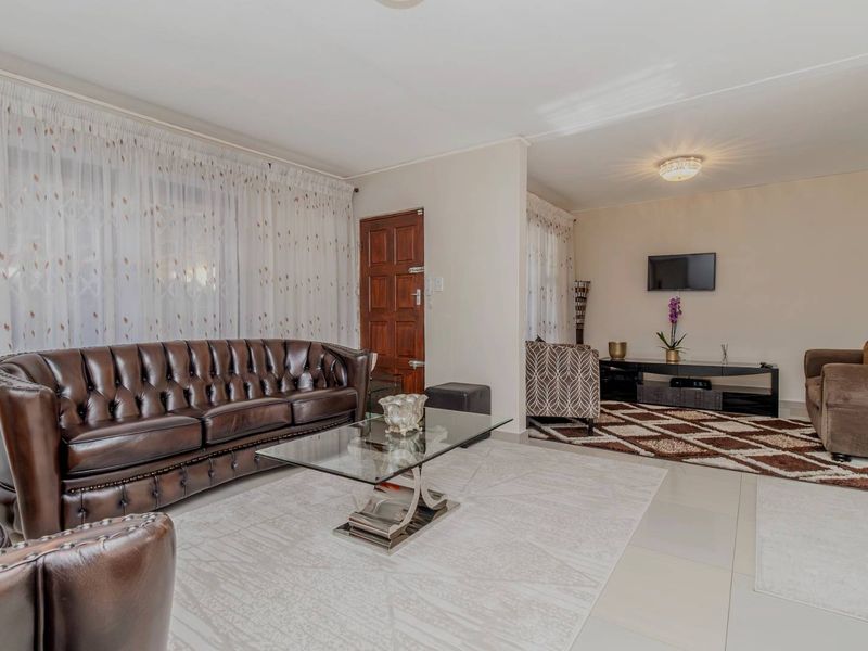 A spacious living area featuring tiled flooring, neutral walls, and a timber entrance door, offering a functional and well-lit layout.