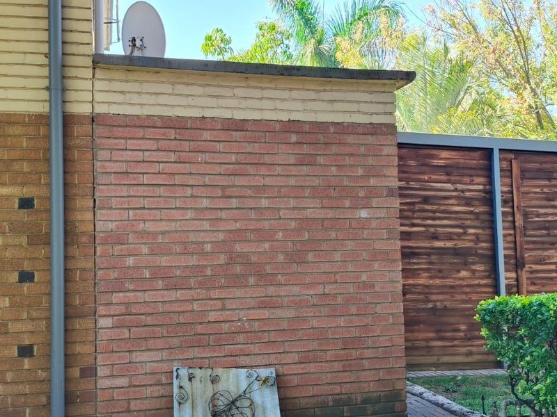 Rear exterior view of the property featuring a brick facade, timber fencing, and a paved walkway area.