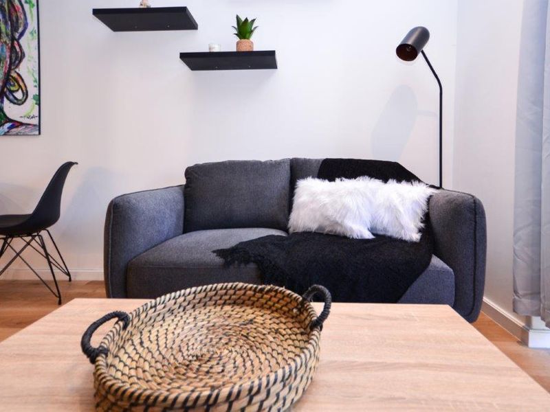A modern living room area featuring light wood-tone laminate flooring and minimalist black floating wall shelves.