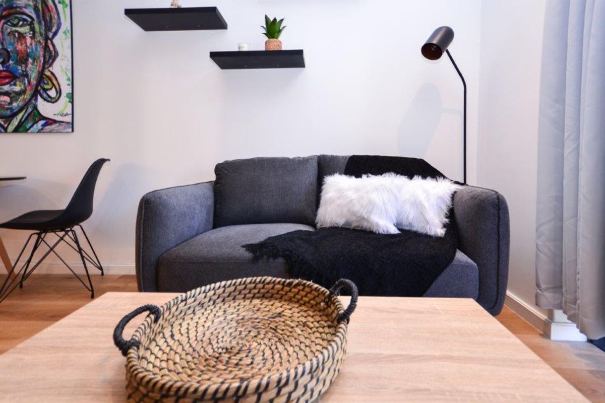 A modern living room area featuring light wood-tone laminate flooring and minimalist black floating wall shelves.