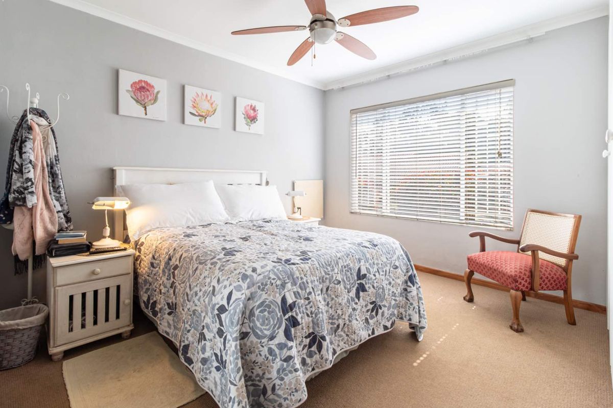 A well-lit bedroom featuring neutral wall tones, carpeted flooring, a ceiling fan, and venetian blinds for adjustable natural light.