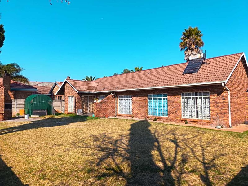 Rear view of a face brick house featuring a tiled roof, solar water heater, security bars on windows, and a built-in outdoor braai area.