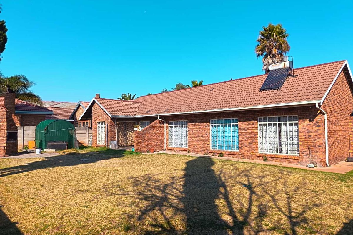 Rear view of a face brick house featuring a tiled roof, solar water heater, security bars on windows, and a built-in outdoor braai area.