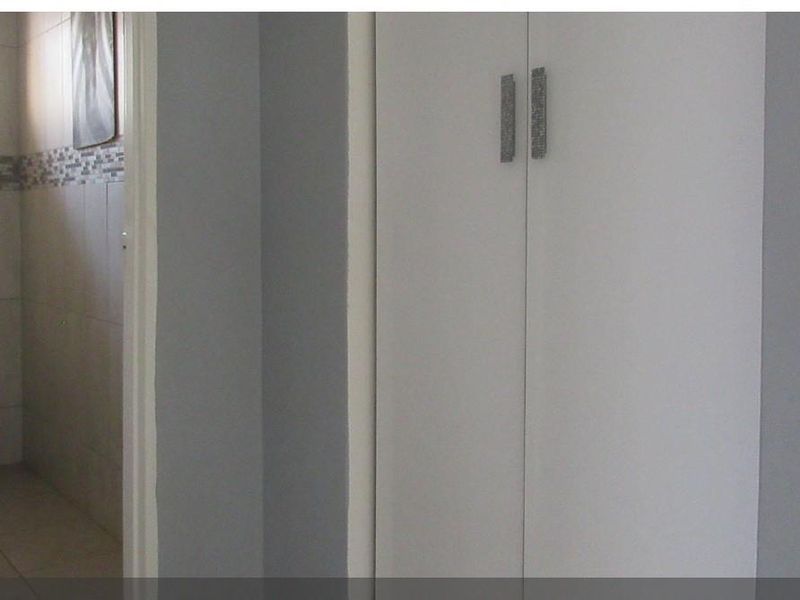 A clean bathroom featuring a wall-mounted toilet, tiled finishes, and built-in storage cupboards in the adjacent hallway area.