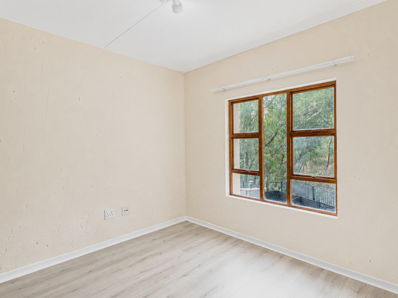 An empty bedroom featuring light-toned laminate flooring, textured walls, and a wooden-framed window overlooking greenery.