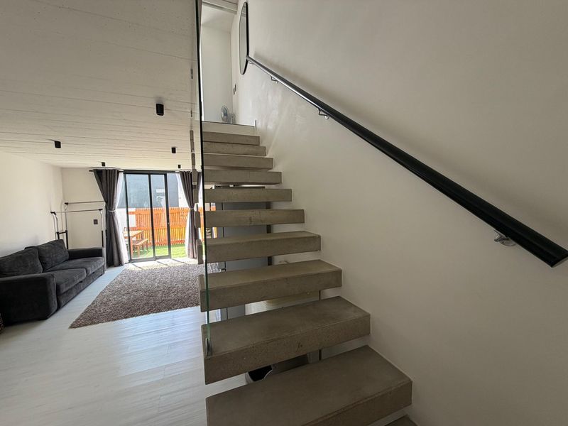 Modern open-plan living area featuring a striking concrete staircase with glass balustrade, leading to an outdoor patio through sliding glass doors.