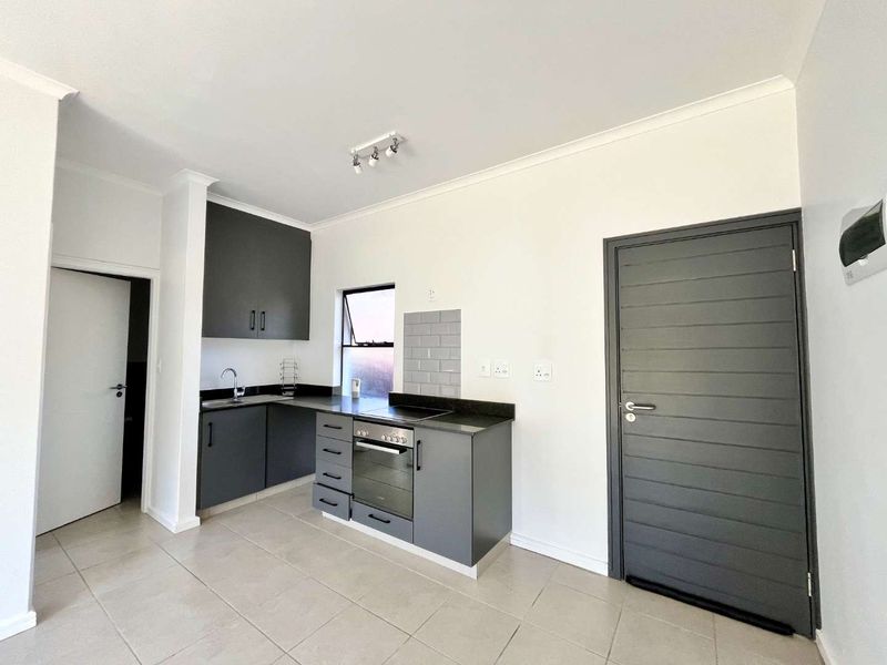 Modern kitchen featuring dark grey cabinetry, stone countertops, built-in oven, hob, and neutral floor tiling in a clean, open-plan layout.