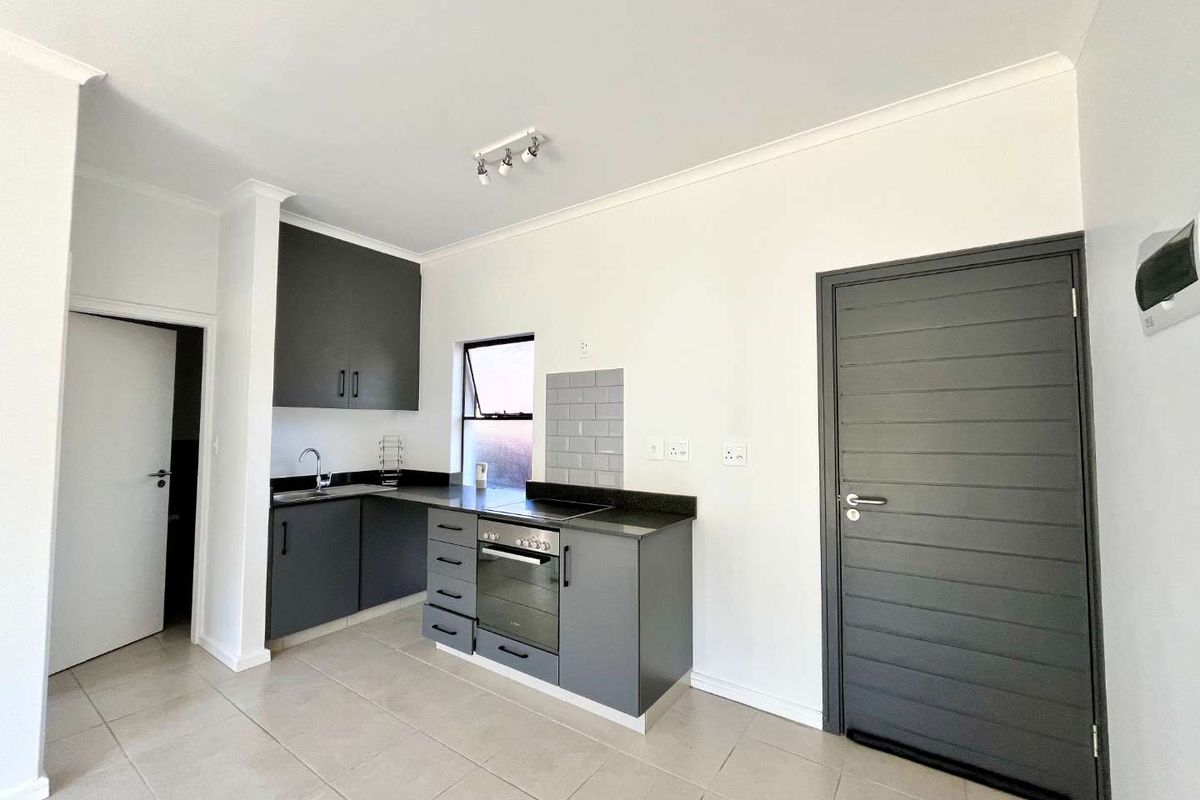 Modern kitchen featuring dark grey cabinetry, stone countertops, built-in oven, hob, and neutral floor tiling in a clean, open-plan layout.