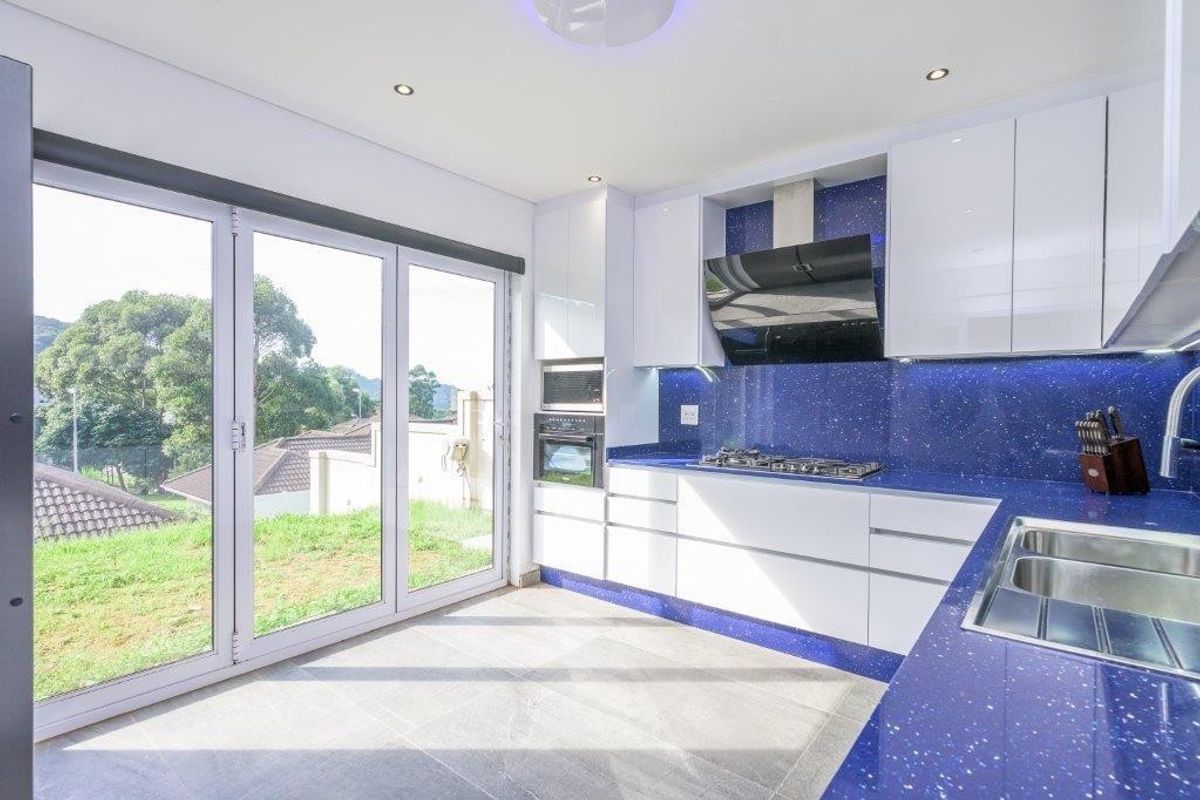 Modern kitchen featuring high-gloss white cabinetry, striking blue stone countertops, integrated appliances, and large sliding glass doors providing natural light and garden access.