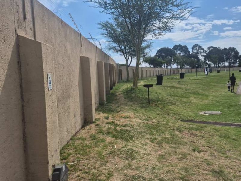 A large, open communal garden area featuring a long perimeter wall with electric fencing and basic drainage infrastructure.