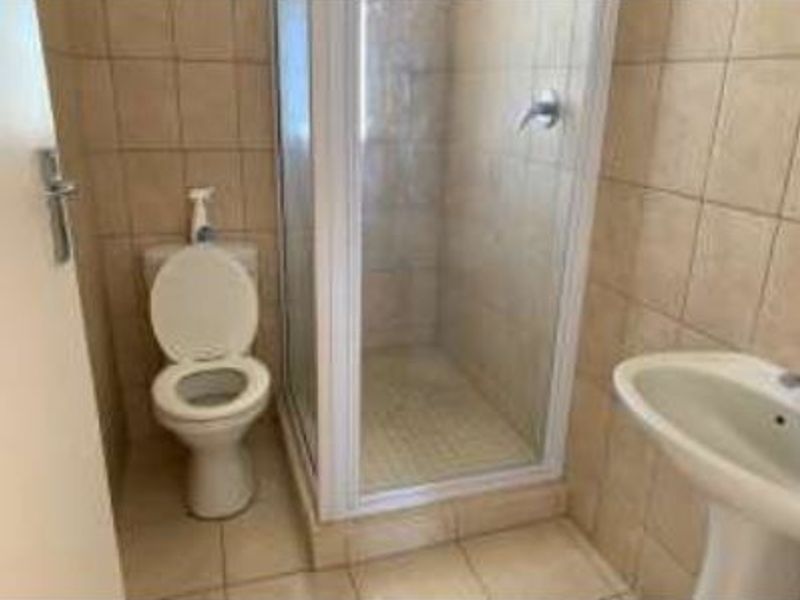 A functional bathroom featuring a shower enclosure, pedestal basin, and toilet with neutral wall and floor tiling.