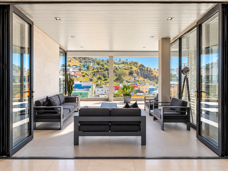 A spacious covered balcony featuring large folding glass doors, stone wall accents, and recessed lighting, offering expansive views of the surrounding landscape.
