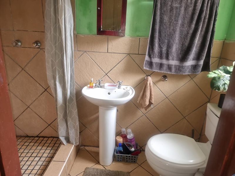 A functional bathroom featuring a pedestal basin, toilet, and shower area with tiled walls and flooring, requiring cosmetic updates to modernize the space.