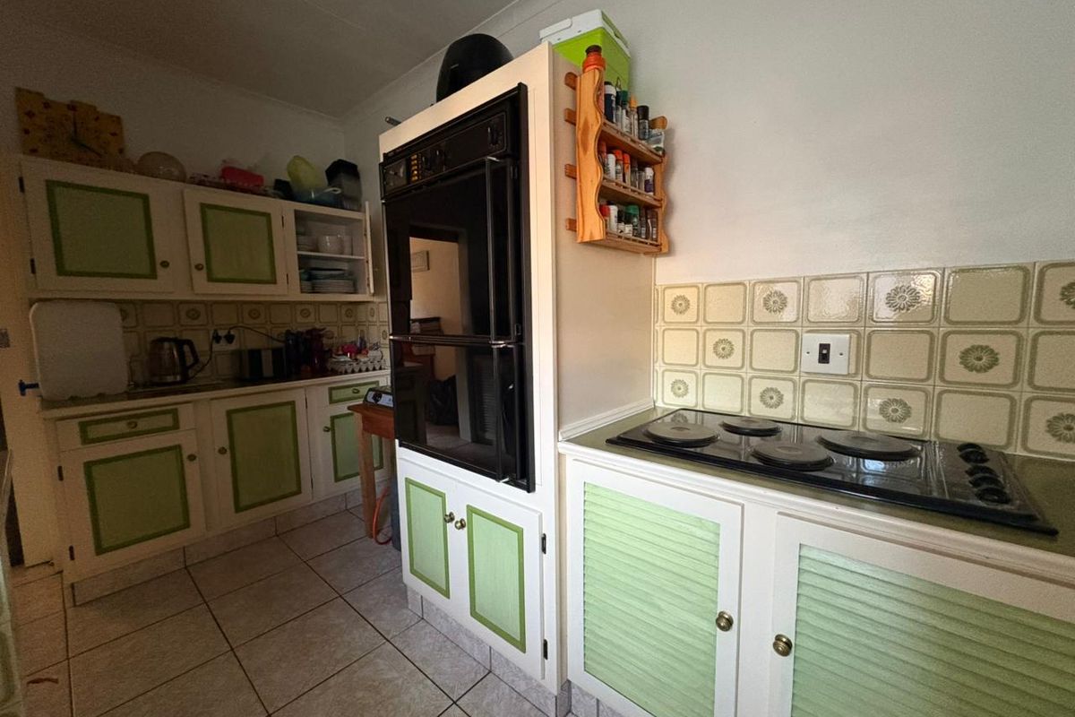 A dated kitchen featuring built-in cabinetry, a wall-mounted oven, and a ceramic hob with a decorative tiled backsplash.