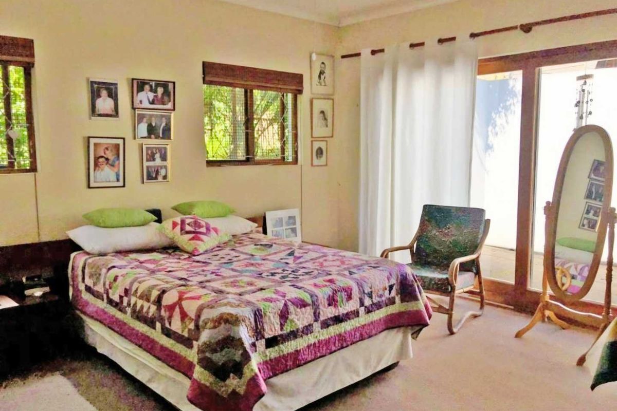 A bedroom featuring carpet flooring, timber window frames, and a sliding glass door providing access to the exterior.