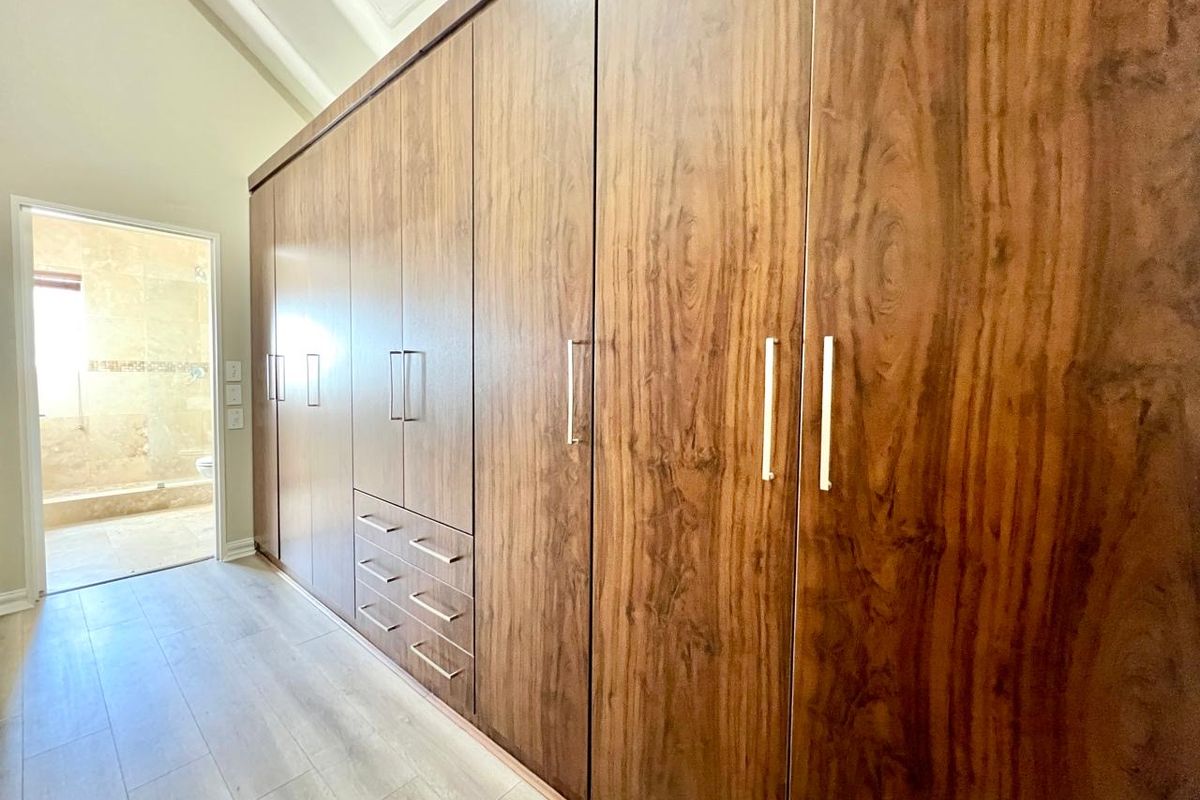 Spacious bedroom featuring extensive floor-to-ceiling built-in wooden cupboards, light laminate flooring, and a vaulted ceiling, with direct access to an en-suite bathroom.