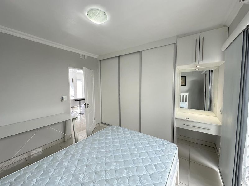 A well-maintained bedroom featuring built-in sliding door wardrobes, a dedicated vanity area, and neutral tiled flooring.