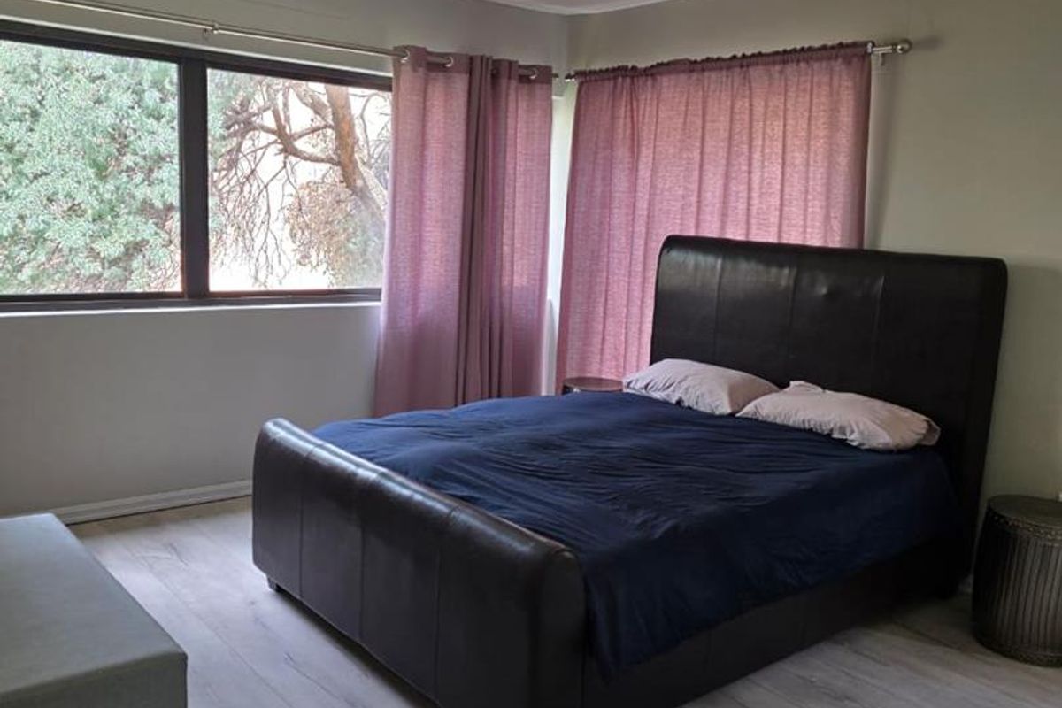 A spacious bedroom featuring light-toned laminate flooring, recessed ceiling lighting, and a large window providing natural light.