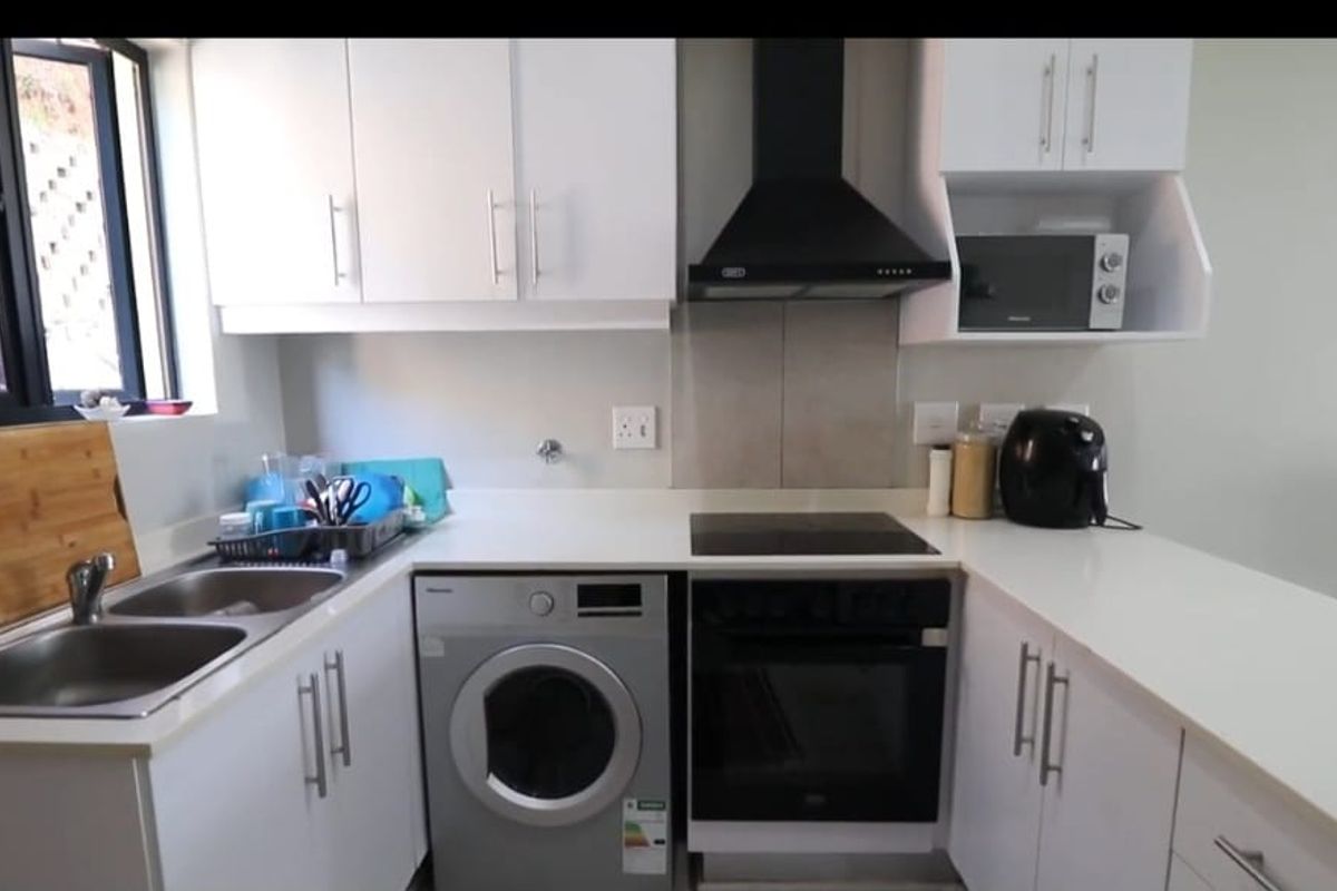 Modern kitchen featuring white cabinetry, stone countertops, integrated oven, electric hob, extractor fan, and a double stainless steel sink.