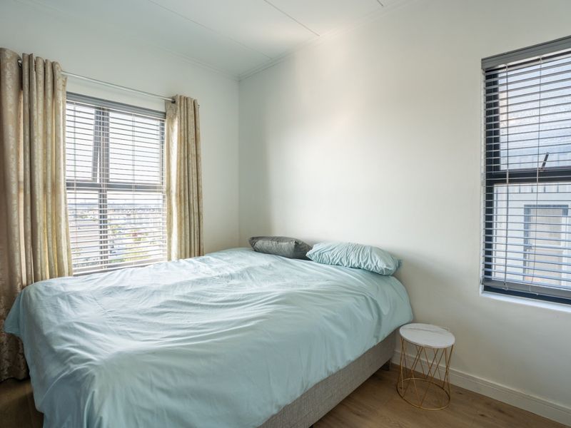 A bright bedroom featuring laminate flooring, dual windows with fitted venetian blinds, and neutral wall finishes.