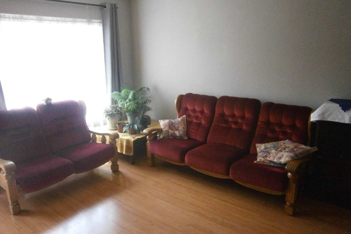 A living room featuring laminate flooring and a large window with a curtain rod, providing natural light to the space.
