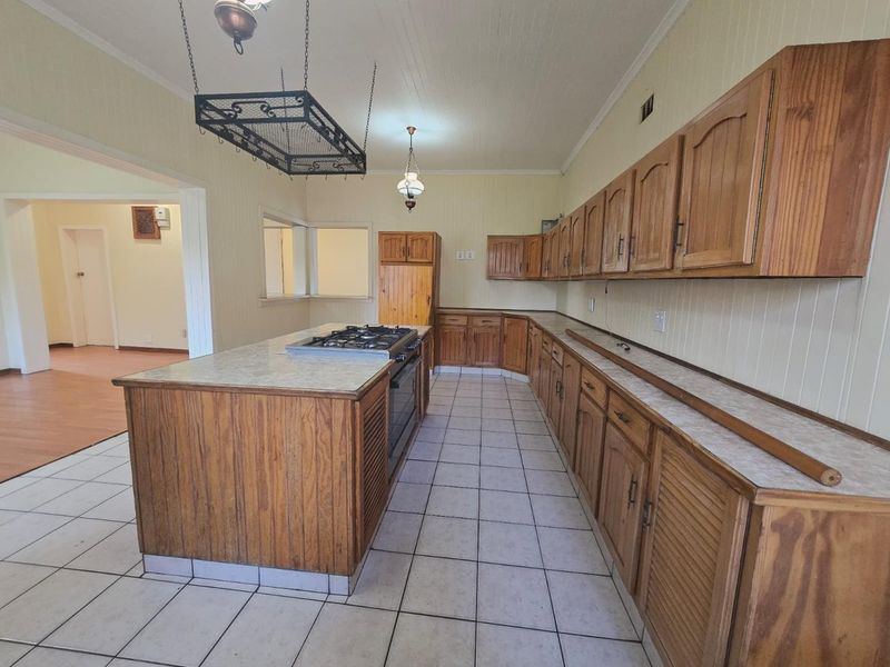 Spacious kitchen featuring extensive wooden cabinetry, a central island with a built-in gas cooktop, and ceramic tiled flooring.