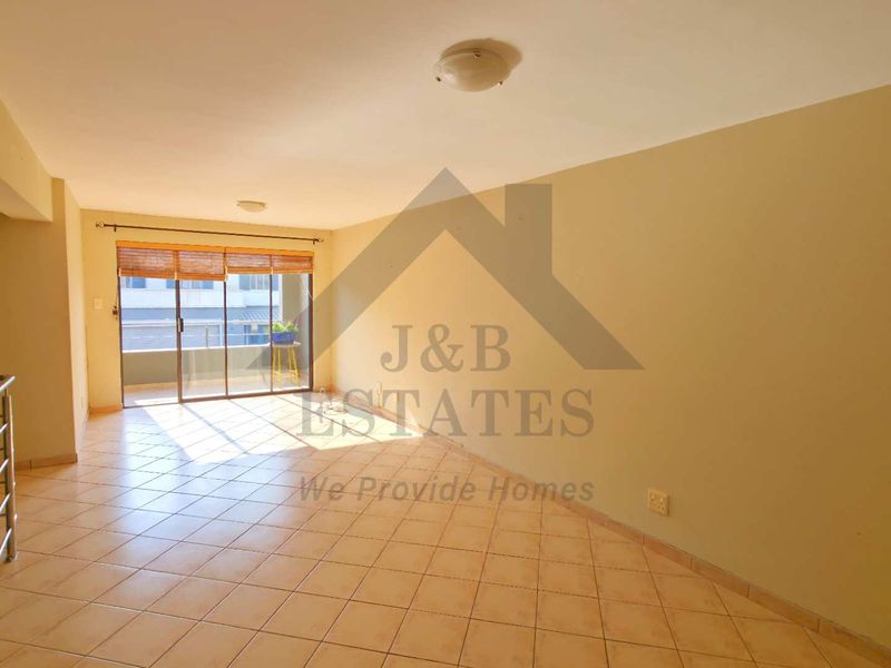 A spacious, empty living area featuring tiled flooring, neutral walls, and a sliding glass door leading to an outdoor balcony.