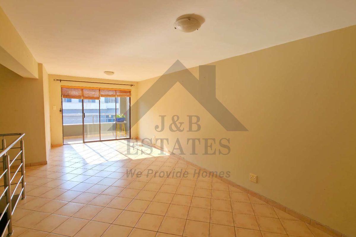 A spacious, empty living area featuring tiled flooring, neutral walls, and a sliding glass door leading to an outdoor balcony.