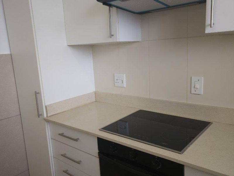 A clean, modern kitchen featuring white cabinetry, stone countertops, a built-in oven, electric hob, and an extractor fan.