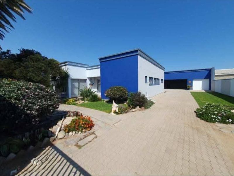 Front exterior view of a modern house featuring a bold blue facade, paved driveway, and well-maintained garden area.