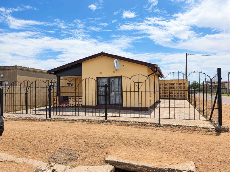Front view of a detached house featuring a paved driveway, wrought iron perimeter fencing, and a covered patio area.