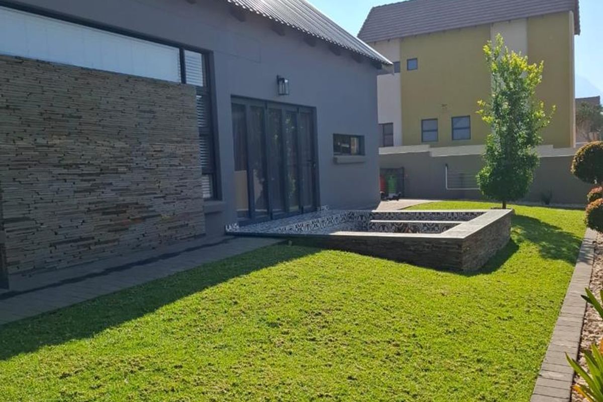 A well-maintained rear garden featuring a manicured lawn, a built-in stone-clad fire pit area, and modern exterior finishes on the house facade.