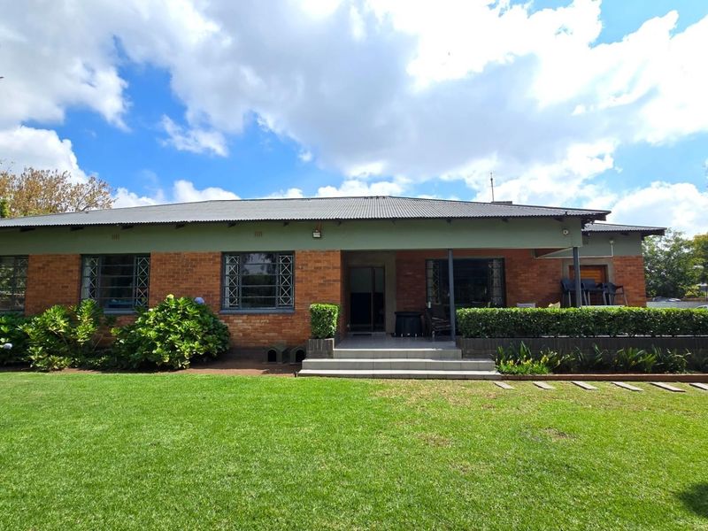 Rear view of a single-story brick house featuring a corrugated metal roof, security-barred windows, and a well-maintained lawn with a paved entrance step.