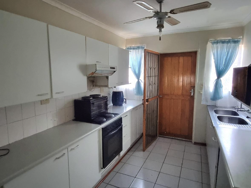 A functional kitchen featuring white cabinetry, double basin sink, built-in oven, and tiled flooring with direct access to the exterior.