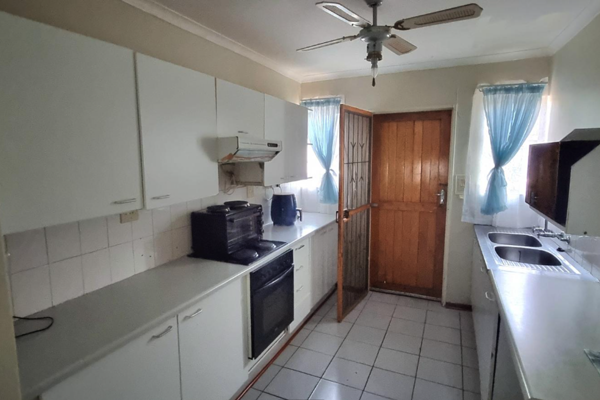 A functional kitchen featuring white cabinetry, double basin sink, built-in oven, and tiled flooring with direct access to the exterior.