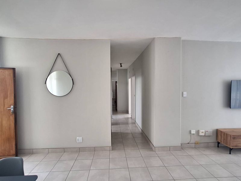A neutral living area featuring tiled flooring and a central hallway leading to other parts of the apartment.