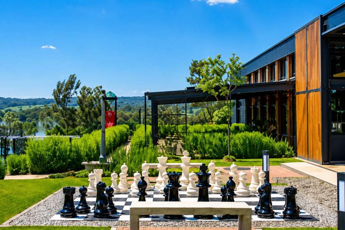 A beautifully landscaped outdoor area featuring a large garden chess set, paved pathways, and modern architectural elements with timber cladding overlooking a scenic landscape.