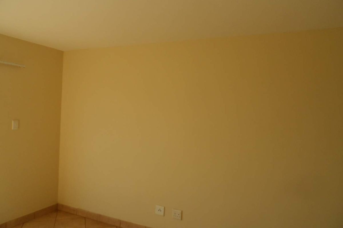 An empty bedroom featuring neutral-toned walls, tiled flooring, and standard electrical fixtures, providing a blank canvas for interior design.